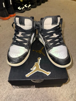 Svarta och vita Air Jordan 1 sneakers - Säljer ett par Air Jordan 1 sneakers i svart och vitt läder med klassisk Nike Swoosh och högt skaft. Skorna har svarta snören och detaljer i elefantmönster på Swoosh och runt snörningen. Perfekta för dig som gillar streetwear och ikoniska sneakers.