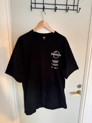 Svart oversized t-shirt med tryck - Cool svart t-shirt med stort tryck av en brinnande basketkorg och texten 'INFINITE' på ryggen. Framsidan har mindre tryck med baskettema. Oversized passform och korta ärmar, perfekt för en avslappnad streetwear-look.