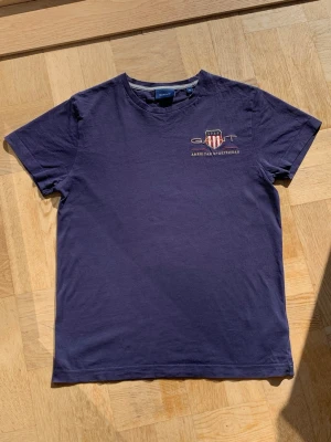 Mörkblå t-shirt från Gant - Snygg mörkblå t-shirt från Gant med broderad logga och texten 'American Sportswear' på bröstet. Klassisk rund hals och korta ärmar. Perfekt till jeans eller shorts för en avslappnad stil.
