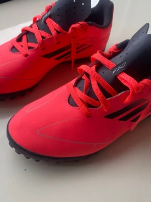 Röda Adidas F50 fotbollsskor - Säljer ett par röda Adidas F50 fotbollsskor med svarta detaljer och klassiska tre ränder på sidan. Skorna har snörning, låg profil och tålig yttersula med dobbar för bra grepp på planen. Perfekta för dig som vill sticka ut på fotbollsplanen.storleken är 38 och kan även användas inne och på gruset 