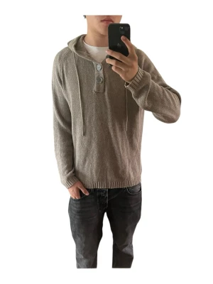 Beige stickad hoodie med knappar - Modellen i bilden är 180cm och väger 69kg. Säljer en beige stickad hoodie med tre knappar vid halsen och dragsko i huvan. Tröjan har långa ärmar och ribbade muddar vid ärmslut och nederkant. Perfekt för dig som gillar en avslappnad och stilren look.
