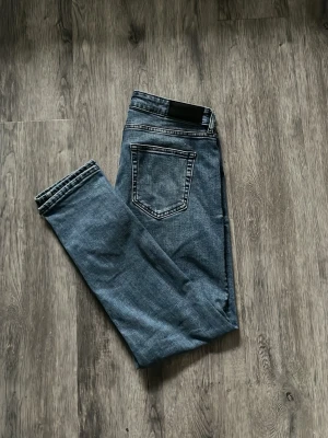 Blå raka jeans med bakficka - Säljer ett par klassiska blå jeans med rak passform och en tydlig bakficka. Jeansen har en enkel design utan slitningar och är tillverkade i ett mjukt denimtyg. Perfekta för en avslappnad och stilren look.