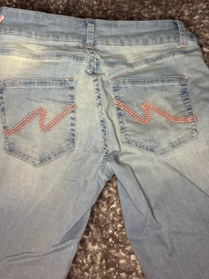 Ljusblå jeans med broderade fickor - Säljer ett par ljusblå jeans med raka ben och snygga broderade detaljer i rosa på bakfickorna. På sista sidan ser ni lite bevis på användning men dessa har jag nästan glömt bort att jag haft köpte dom i november och haft på mig dom en gång under regn, tvättade dom sen aldrig mera dock jätte snygga men också lite för stora!
