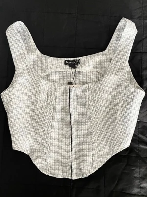Vit rutig korsettopp  - Trendig vit korsettopp med rutigt mönster och breda axelband. Toppen har en strukturerad passform och är perfekt för att lyfta din outfit. Tillverkad i ett lätt och bekvämt material.
