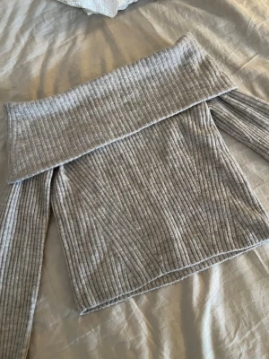 Off shoulder stickad tröja - Trendig ljusgrå/beige stickad tröja med bred off shoulder-krage och ribbad struktur. Långa ärmar och mjukt material.