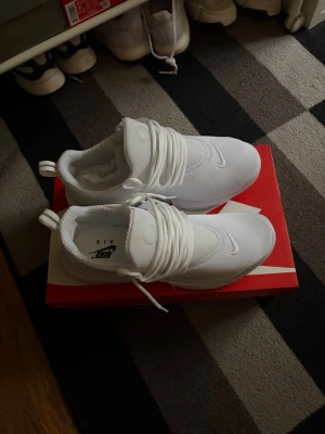Vita Nike Air sneakers - Säljer ett par helvita Nike Air sneakers med låg profil och klassisk swoosh på tån. Skorna har tjocka vita snören, mesh- och textilmaterial samt dragflikar bak för enkel påtagning. Perfekta för dig som gillar stilrena och sportiga sneakers. Obs original förpackning finns inte med men annan Nike låda.