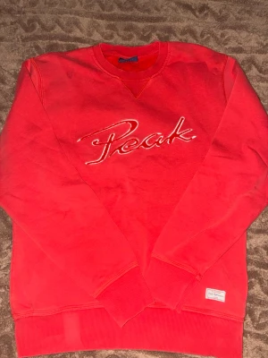 Röd sweatshirt från Peak Performance - Riktigt snygg röd sweatshirt från Peak Performance med broderad logga på bröstet. Klassisk rund halsringning och ribbade muddar vid ärmslut och nederkant. Perfekt för en avslappnad och sportig stil.