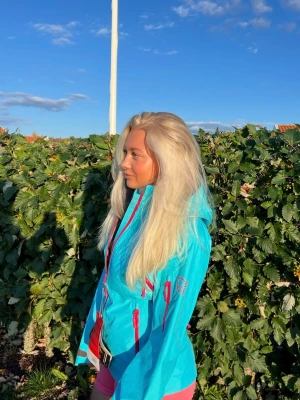 Norrøna, Turkos vind- och vattentät jacka med rosa detaljer - Helt oanvänd Norrøna vind- och vattentät turkos jacka med rosa dragkedjor och detaljer. Jackan har flanell-insida, vilket gör den varmare. Jackan har flera fickor med dragkedja och justerbara ärmslut. Ventilationsdrajkedjor finns längs med sidorna. Perfekt för alpint och outdoor-aktiviteter. 