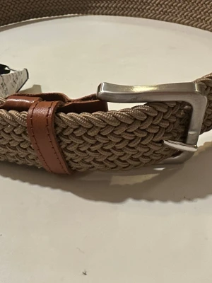 Beige flätat bälte från Jack & Jones - Snyggt beige flätat bälte från Jack & Jones med detaljer i brunt skinn och ett silvrigt metallspänne. Perfekt accessoar för att lyfta din outfit med en stilren och modern touch.