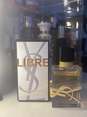 Yves Saint Laurent Libre parfym - Yves Saint Laurent Libre parfym med elegant glasflaska och svart fyrkantigt lock. Flaskan har guldiga detaljer och en stor YSL-logga runt om. Förpackningen är vit med guldtext och YSL-logga. En lyxig och modern doft.