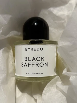 Byredo Black Saffron Eau de Parfum – 50 ml - En varm, elegant och karaktärsfull unisexdoft med både kryddiga, fruktiga och läderaktiga toner. Öppnar med saffran, enbär och pomelo, följt av svart viol, ros och läder. Basen rundas av med hallon, ljusa tränoter och vetiver. Byredo beskriver den som intensiv, amberaktig och genderless.   Ca 70–75 % kvar – se bild för aktuell nivå. Säljs utan originalkartong.