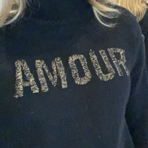 Zadig Voltaire Amour tröja - Snygg svart tröja med texten 'AMOUR' i glittriga bokstäver på framsidan. Tröjan har en hög krage och knappar på axeln för en extra detalj. Perfekt för en stilren look. Den sitter som en S i dam storlek passar mig perfekt som är 165