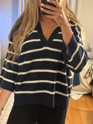 Marinblå stickad tröja med ränder - Säljer en marinblå stickad tröja med vita horisontella ränder. Tröjan har en djup V-ringning och trekvartsärmar. Den är oversized och mjuk, perfekt för lager på lager. Passar dig som gillar en avslappnad och trendig stil.