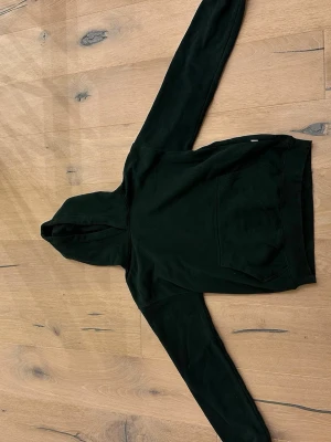  Grön hoodie från Vailent med magficka - En snygg mörk grön hoodie med huva och stor magficka framtill. Hoodien har långa ärmar och ribbade muddar vid ärmslut och nederkant. Perfekt för en avslappnad och stilren look.
