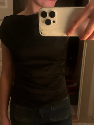 Svart tight satin topp med kort ärm - Snygg svart topp med tight passform och korta ärmar. Enkel och stilren design som passar till det mesta. Tillverkad i ett stretchigt material som sitter skönt på kroppen.