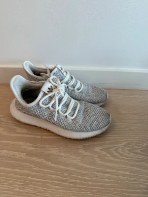 Gråvita Adidas sneakers i mesh - Säljer ett par gråvita Adidas sneakers med stickad mesh-överdel och vita snören. Skorna har en chunky vit sula och den klassiska Adidas-loggan på plösen. Perfekta för dig som gillar sportig och clean stil.
