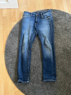 Blå jeans från Jack & Jones - Snygga blå jeans från Jack & Jones i modellen Regular Clark. Jeansen har en klassisk femficksdesign, normal passform och lätt slitna detaljer framtill för en avslappnad look. Perfekta till vardags och passar till det mesta i garderoben.