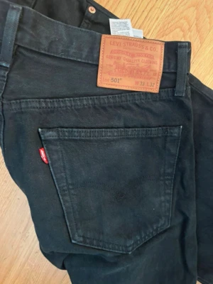 Svarta Levi's 501 jeans W33 L32 - Säljer ett par klassiska svarta Levi's 501 jeans i modellen Premium. Jeansen har raka ben, fem fickor och den ikoniska röda Levi's-lappen på bakfickan. Tillverkade i slitstark denim med snygga detaljer och läderpatch bak.