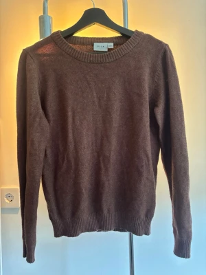 Brun stickad tröja från VILA - Mysig brun stickad tröja från VILA med rund halsringning och ribbade muddar vid ärmslut och nederkant. Perfekt för lager på lager och enkel att matcha med olika outfits.