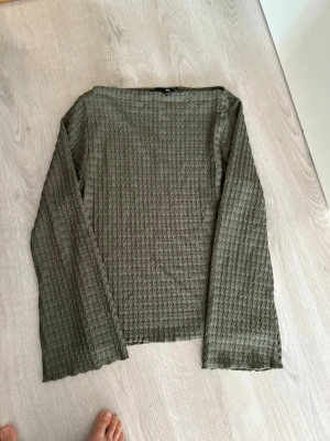Olivgrön ribbad långärmad topp - Säljer en olivgrön långärmad topp med ribbad struktur och vågig kant. Toppen har en rak passform och är tillverkad i ett lätt, stretchigt material som känns skönt mot huden. Perfekt att styla med jeans eller kjol för en trendig look.