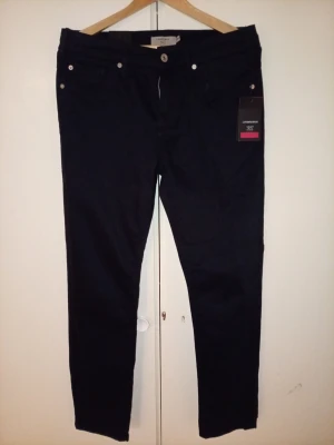 J.Lindebergh Chinos - Snygga Blå chinos från J.Lindebergh med superflex och cashmere touch för extra mjuk känsla. Byxorna har raka ben och klassisk design med bakfickor och bälteshällor. Perfekta för dig som vill ha både stil och komfort. Oanvända 1907 1299 i butik