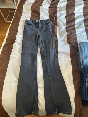 Mörkgrå bootcut jeans - Säljer ett par mörkgrå bootcut jeans med klassisk femficksdesign och dragkedja med knapp. Jeansen har en snygg utsvängd passform och är tillverkade i ett mjukt denimtyg som ger en skön känsla. Perfekta för dig som gillar retrovibbar och vill ha ett par jeans som sticker ut.