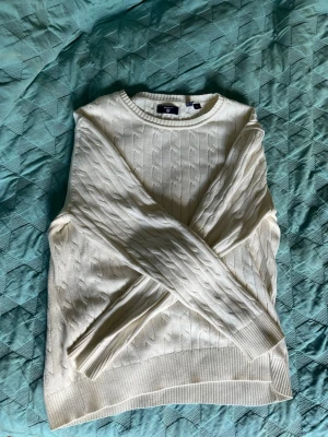 Vit kabelstickad tröja - Kabelstickad vit tröja med rund halsringning och ribbade muddar vid ärmslut och nederkant. Klassisk och stilren design som passar till det mesta. Mjuk och skön, perfekt för lager på lager under kyligare dagar.