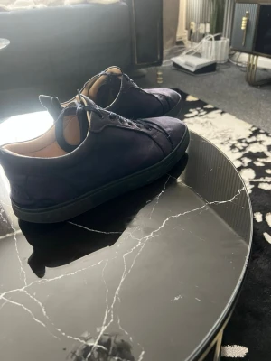 Mörkblå sneakers i mocka - Snygga mörkblå sneakers i mocka med svarta sulor och matchande skosnören. Skorna har en låg profil och diskret broderad text på hälen. Insidan är ljusbeige och designen är stilren och enkel.