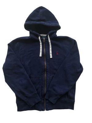 Ralph Lauren Zip Hoodie Mörkblå - Mörkblå hoodie med dragkedja och vit dragsko i huvan. Klassisk design med ribbade muddar och fickor framtill. Liten röd logga broderad på bröstet. Perfekt för en avslappnad och stilren look.