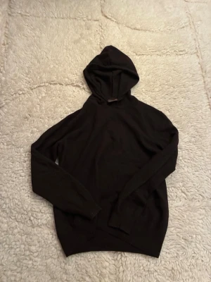 Mörkbrun kashmir hoodie från Osccar Jacobson  - En stilren svart hoodie med huva och långa ärmar. Tröjan är tillverkad i ett mjukt och bekvämt tyg, perfekt för en avslappnad look. Passar dig som gillar enkel och klassisk stil.