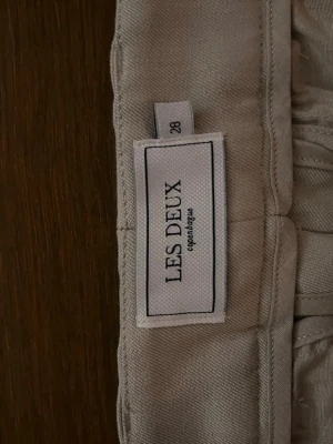 Beige chinos från Les Deux - Snygga beige chinos från Les Deux med klassisk rak passform. Byxorna har diskreta sidofickor, bälteshällor och stängs med dragkedja och två knappar. Perfekta för en clean och stilren look.