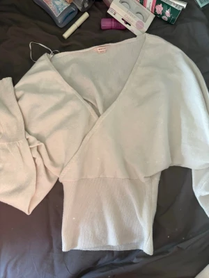 Vit omlottstickad tröja Gina Tricot - Säljer en vit stickad omlott-tröja från Gina Tricot i storlek XS. Tröjan har långa ärmar, bred midjeresår och en djup v-ringning. Perfekt för dig som gillar en enkel men trendig look. Materialet är mjukt och stretchigt.