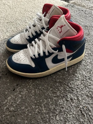 Nike Air Jordan 1 Mid blå/vit/röd - Säljer ett par Nike Air Jordan 1 Mid sneakers i blått, vitt och rött.Bra skick ,hör av er vid frågor😊