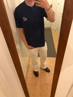 Mörkblå t-shirt med tryck - Säljer en mörkblå t-shirt med coolt vitt tryck på ryggen och mindre tryck på bröstet. T-shirten har rund hals och korta ärmar. Perfekt för dig som gillar streetwear och vill sticka ut lite extra.