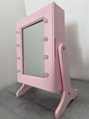Rosa smyckeskrin med spegel & led lampor - Snygg rosa sminkspegel med LED-lampor runt spegelglaset. Spegeln har en rektangulär form och står på ett stabilt stativ. Inuti finns smart förvaring för smycken och accessoarer med krokar och fack. Tillverkad i trä och passar perfekt på sminkbordet. 