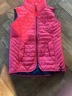 Rosa dunväst/ ridväst från Fouganza - Snygg rosa dunväst från Fouganza med dragkedja framtill och två fickor. Västen har quiltad design och hög krage, perfekt för lager på lager. Tillverkad i lätt och värmande material, passar till många olika outfits. (Tjejen på bilden är 13 år)