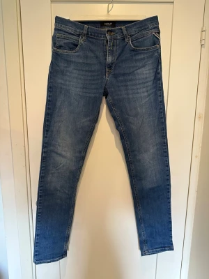 Blå jeans från Replay - Säljer ett par klassiska blå jeans från Replay med fem fickor och raka ben. Jeansen har snygga slitningar och en skön tvättad look. Tillverkade i denim med detaljerade sömmar och Replay-lapp bak i midjan. Det är ett par byxor i barnstorlek.