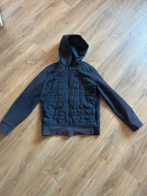 Mörkblå cardigan från Polo Ralph Lauren - Snygg mörkblå cardigan från Polo Ralph Lauren med quiltad framsida och dragkedja. Klassisk huva med dragsko och broderad logga på bröstet. Ärmar och rygg i mjuk sweatshirtmaterial, perfekt för en chill look.