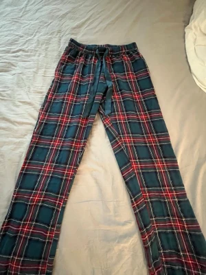 Rutiga pyjamassett  i blått och rött - Klassisk tvådelad pyjamas med långärmad skjorta och byxor i mjukt tyg. Setet har blå bas med rött och vitt rutmönster, settet saknar en knapp längst upp på tröjan men inget som förstör 