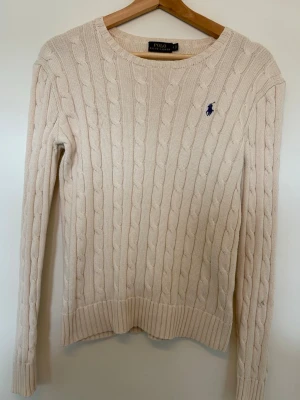Beige kabelstickad tröja Polo Ralph Lauren - Kabelstickad tröja från Polo Ralph Lauren i storlek S. Tröjan är i bra skick, men har några små fläckar på baksidan. (Se bild) 