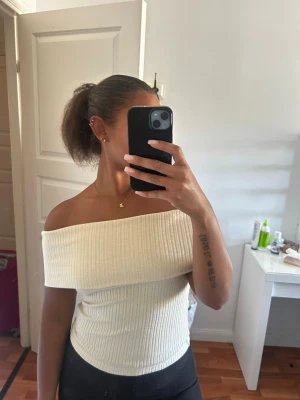 Offshoulder ribbad topp i ljus beige - Säljer en snygg offshoulder topp i ljus beige med ribbad struktur. Toppen är axelbandslös och har en tight passform och mjukt material. Perfekt för dig som vill ha en stilren och kvinnlig look.