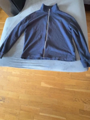 Mörkblå ziptröja med krage - En enkel och stilren mörkblå ziptröja med hög krage och långa ärmar. Tröjan har dragkedja framtill och är tillverkad i ett mjukt bomullsliknande material. Perfekt att slänga på sig när det är lite kyligt ute.