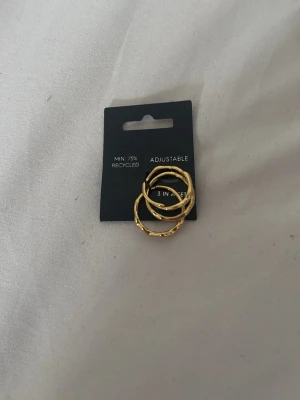 Guldiga justerbara ringar 3-pack pilgrim - Säljer ett set med tre guldiga ringar.  Ringarna är justerbara och har en modern, lite ojämn design som ger en trendig look. Tillverkade av minst 75% återvunnet material. Helt oanvända och kostar originellt 449kr