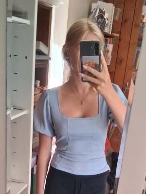 Ljusblå ribbad topp med fyrkantig ringning - Säljer en ljusblå ribbad topp med korta ärmar och snygg fyrkantig ringning. Toppen har en croppad passform och är gjord i mjuk bomull, perfekt för en trendig och avslappnad stil. Superfin och elegant passar till allt. 
