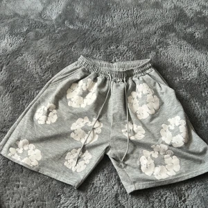 Grå blommiga shorts från Denim Tears - Snygga grå shorts från Denim Tears med vita blommönster över hela plagget. De har elastisk midja med snörning och en bakficka. Perfekta för chill dagar och sommar vibes.