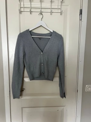 Ljusblå kofta från H&M med pärlknappar - Supersöt ljusblå kofta från H&M med v-ringning och dekorativa pärlknappar framtill. Modellen är croppad med långa ärmar och ribbade muddar. Perfekt att slänga över en topp för en chill look.