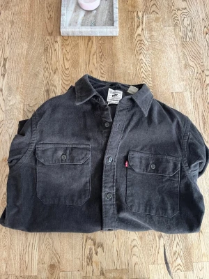 Svart manchester overshirt från Levi's - Säljer en svart/grå overshirt från Levi's i manchestertyg, modell Jackson Worker Relaxed. Skjortan har två stora bröstfickor med knappar och klassisk krage. Använd 1 till 2 gånger