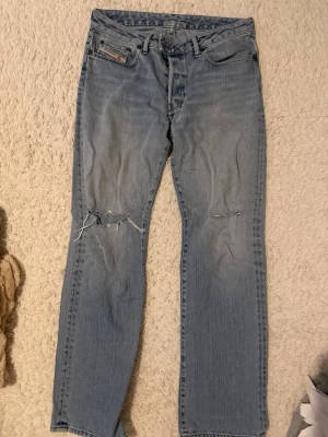 Ljusblå raka jeans  - Säljer ett par ljusblå raka jeans med slitningar och hål på båda benen. Klassisk femficksmodell med knappgylf och detaljerade sömmar. Perfekta för en avslappnad och trendig look. Storlek står inte men jag bär M/38 i byxor och dessa passar mig.