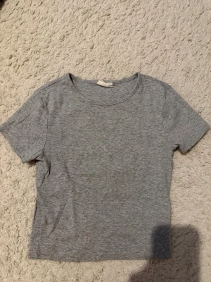 Grå basic t-shirt från Gina Tricot  - En enkel och stilren grå t-shirt från Gina Tricot, perfekt till alla outfits. Modellen är kortärmad med rund halsringning och tillverkad i mjuk bomull. Passformen är normal och tyget är tunt och bekvämt. Använt två gånger 