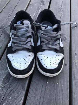 Nike panda dunks - Säljer ett par klassiska svartvita Nike sneakers med lågt skaft. Skorna har gråa skosnören, vit tåbox med perforeringar och svart ovandel i läder. Perfekta för dig som gillar streetwear och vill ha en tidlös look.